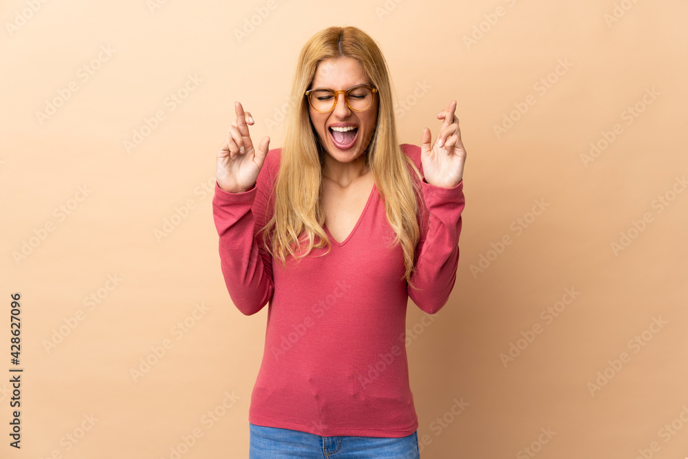 Young Uruguayan blonde woman over isolated background with fingers crossing Young Uruguayan blonde woman over isolated background with fingers crossing