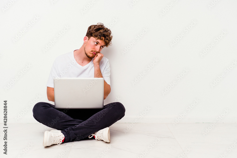 Young caucasian man sitting on the floor holding on laptop isolated on white background who feels sad and pensive, looking at copy space. Young caucasian man sitting on the floor holding on laptop isolated on white background who feels sad and pensive, looking at copy space.