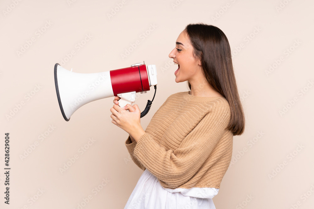 Young caucasian woman isolated on beige background shouting through a megaphone Young caucasian woman isolated on beige background shouting through a megaphone