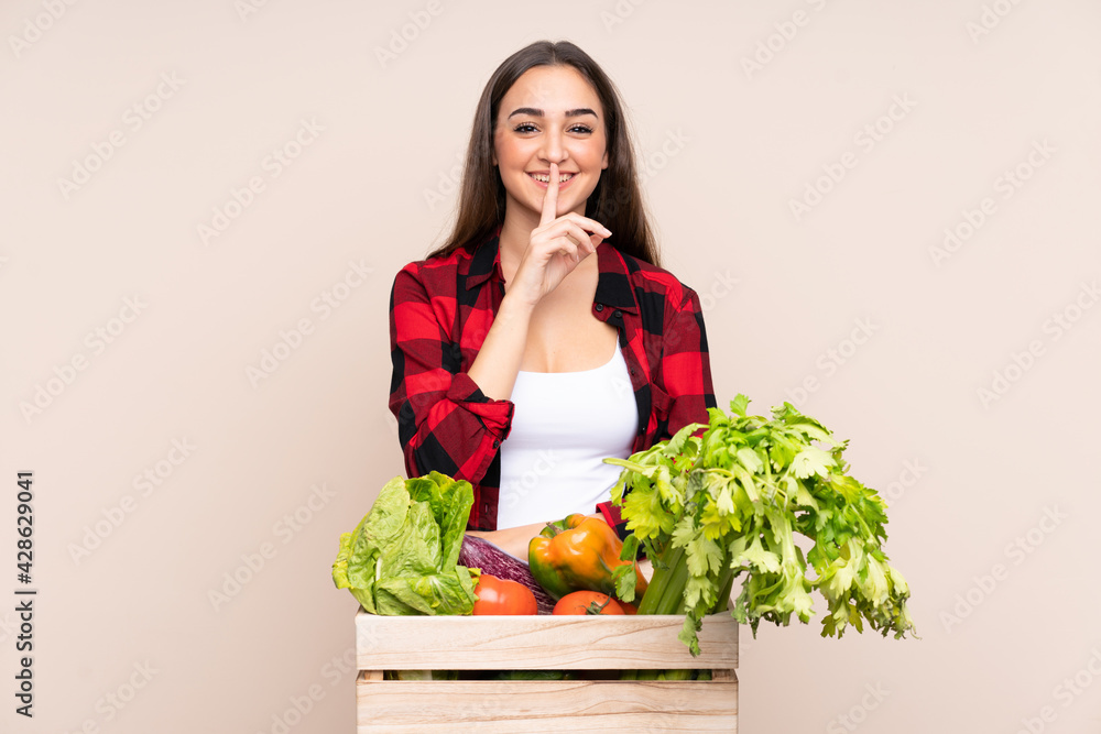 Farmer with freshly picked vegetables in a box isolated on beige background doing silence gesture Farmer with freshly picked vegetables in a box isolated on beige background doing silence gesture
