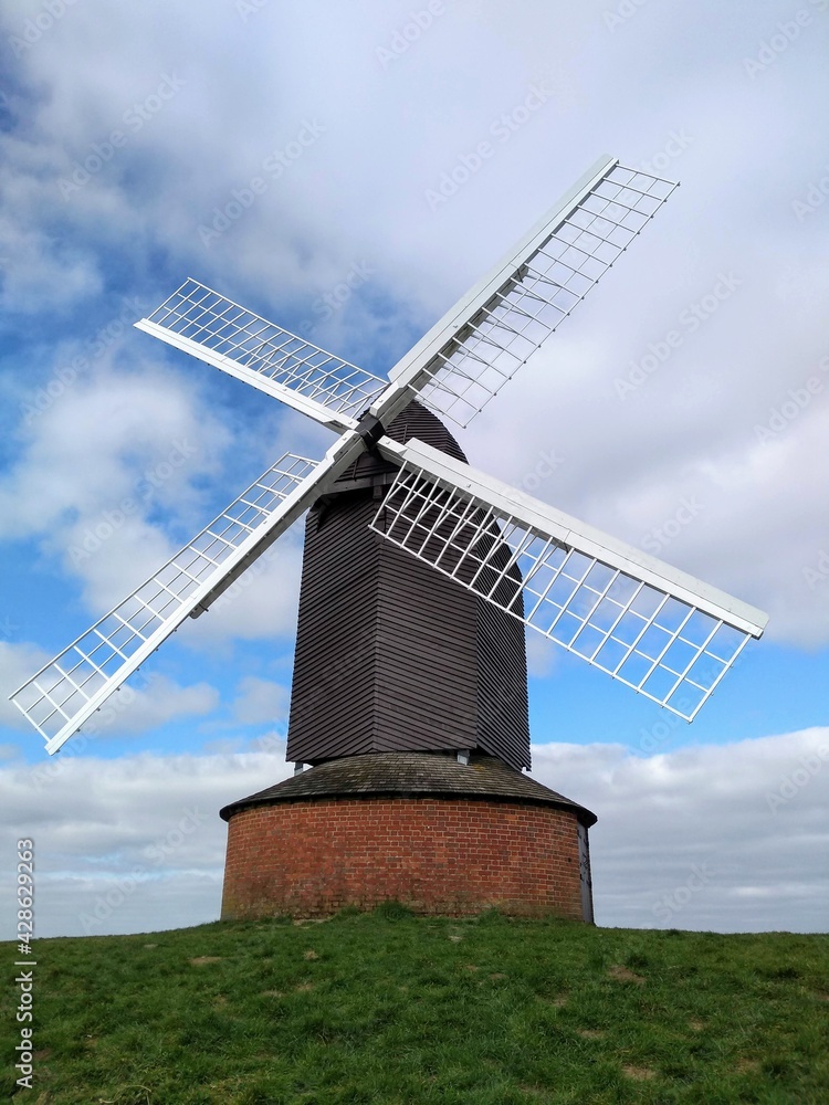 A windmill on a hill in Brill near Aylesbury in Buckinghamshire. The sails of the windmill are shown against a blue sky with white clouds.