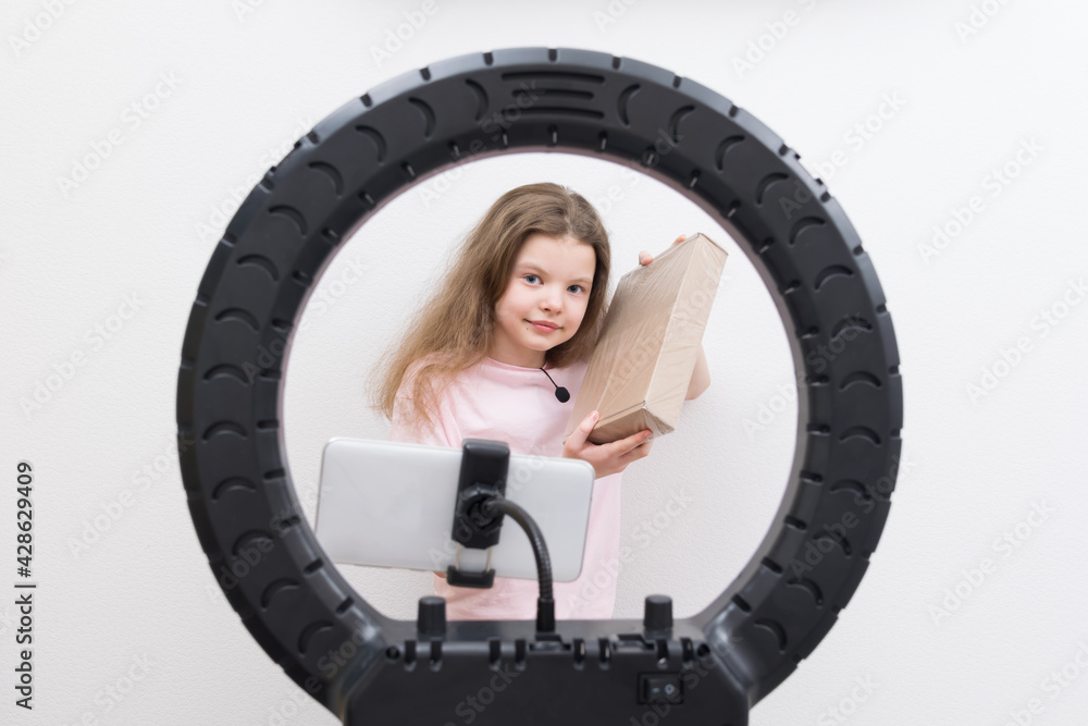 Fototapeta premium a girl blogger, in the center of a circular lamp and a smartphone, makes a review of the package for unpacking