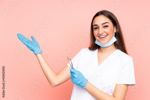 Woman dentist holding tools isolated on pink background extending hands to the side for inviting to come