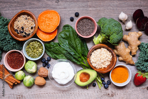 Group of healthy food ingredients. Top view table scene on a wooden background. Super food concept with green vegetables, berries, whole grains, seeds, spices and nutritious items.
