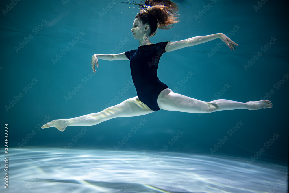  beautiful girl in a black leotard doing gymnastic exercises underwater on a blue background 