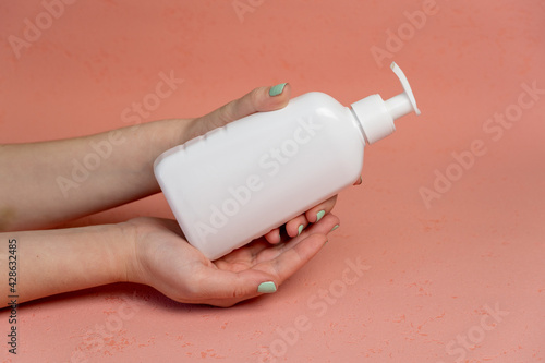 Pump plastic bottle for intimate gel dispenser or liquid soap in the hands on pink background
