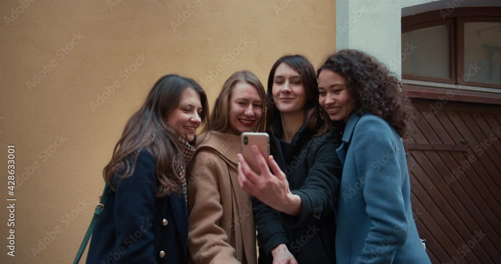Group of beautiful multiethnic happy young women smiling together for selfie picture using smartphone at beige building. Group of beautiful multiethnic happy young women smiling together for selfie picture using smartphone at beige building.