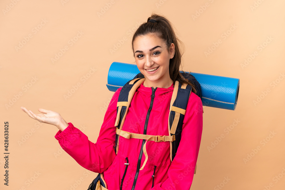 Young mountaineer girl with a big backpacker isolated on beige background holding copyspace imaginary on the palm Young mountaineer girl with a big backpacker isolated on beige background holding copyspace imaginary on the palm