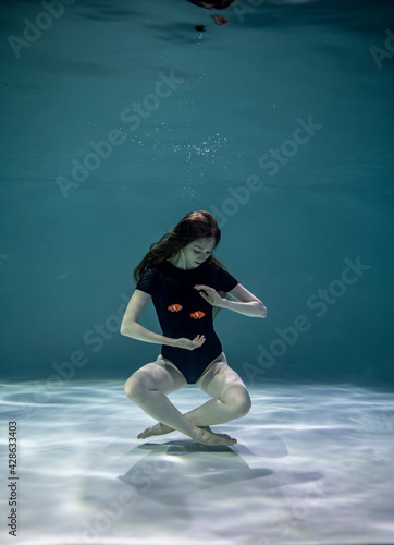 beautiful girl in a black swimsuit plays in orange fish underwater on a blue background 