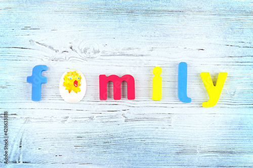 The word "Family", made of multi-colored wooden letters and chick hatched from an egg on a painted wooden background. Family symbol. Concept happy family. Birth concept. Copy space. Top view.