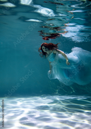  beautiful woman with red hair in a lush blue dress posing underwater 