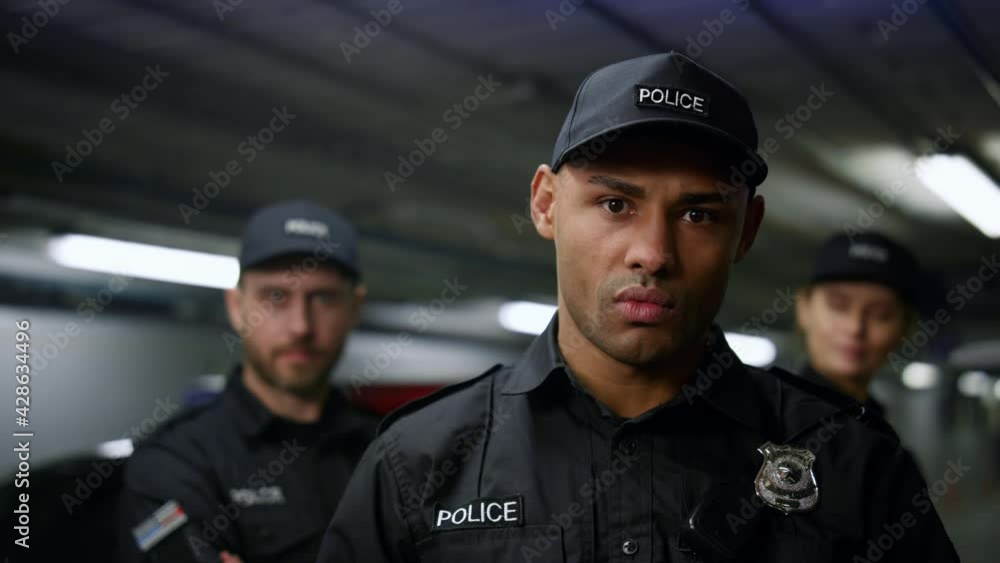 Policeman posing at camera. Police officer in cap standing at patrol car Policeman posing at camera. Police officer in cap standing at patrol car