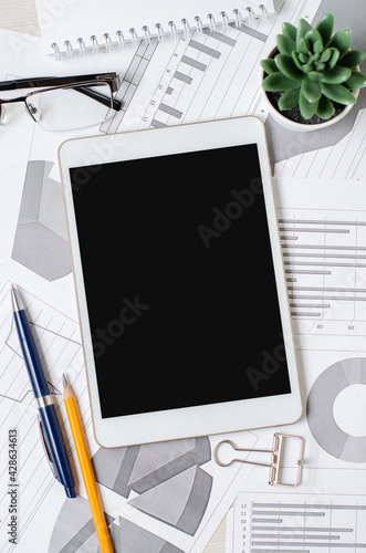 Tablet with a blank screen on the background of charts and graphs. The concept of online investing or business processes. Copy space