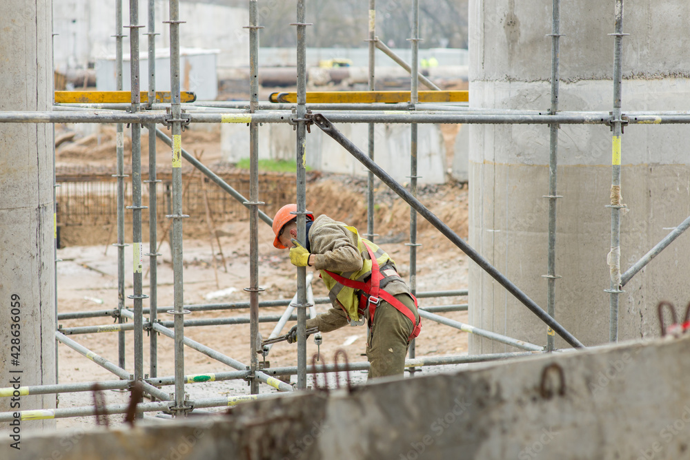 Builder assembles scaffolding at construction site,