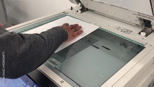 Man's hand adjusting the paper or document on a copier xerox machine to make a copy
