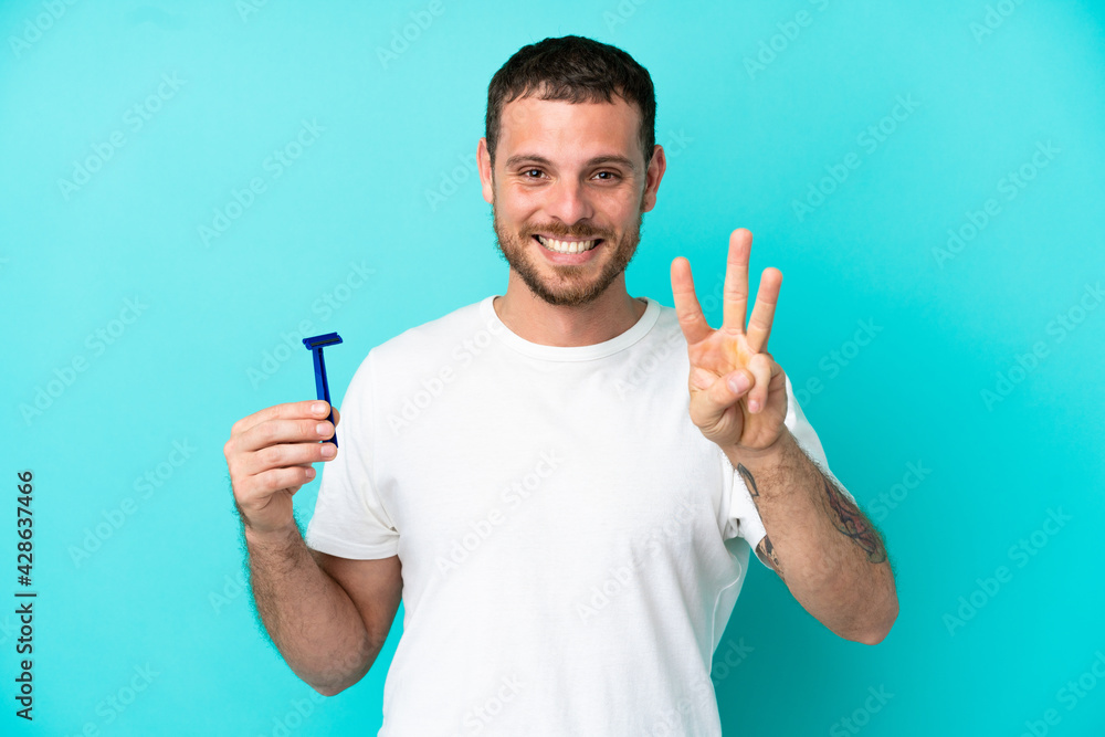 Fototapeta premium Brazilian man shaving his beard isolated on blue background happy and counting three with fingers