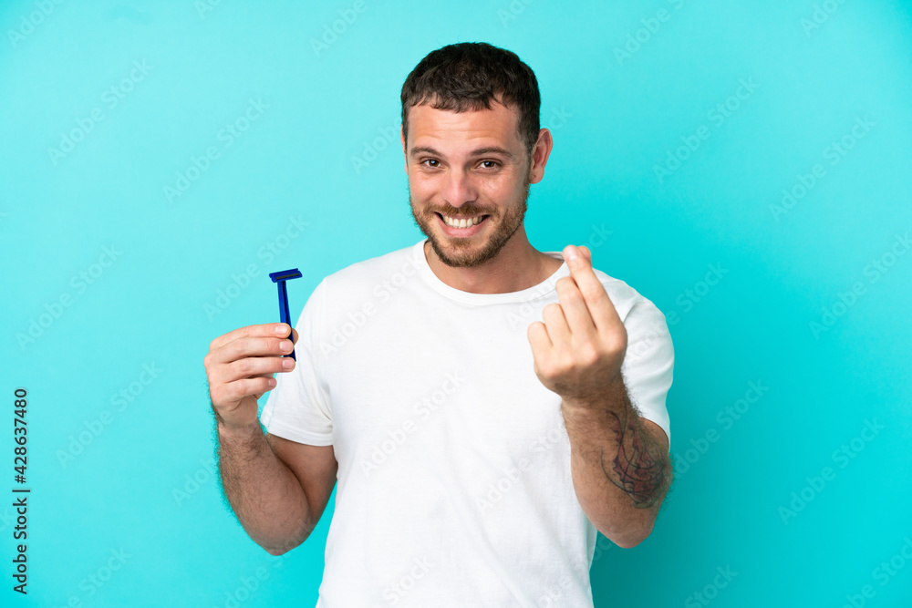 Fototapeta premium Brazilian man shaving his beard isolated on blue background making money gesture