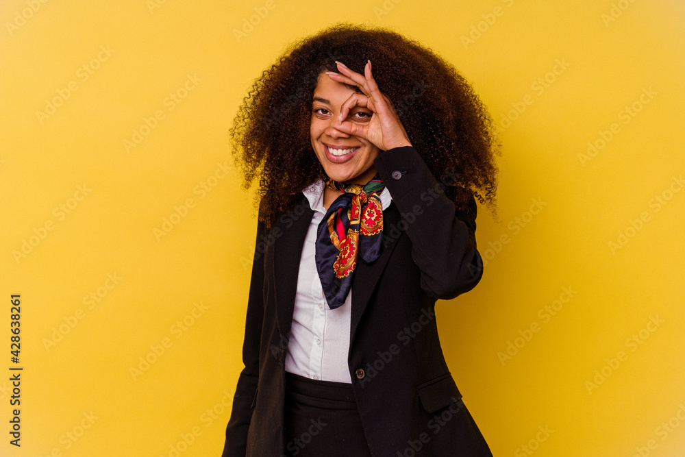Young African American air hostess isolated on yellow background excited keeping ok gesture on eye. Young African American air hostess isolated on yellow background excited keeping ok gesture on eye.