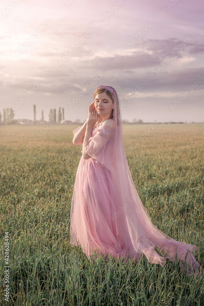 girl stands on a spring field in the rays of the setting sun