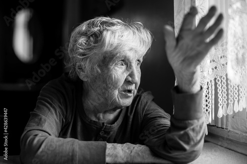 The old woman talking gesticulating at the table in her home. Black and white photo.