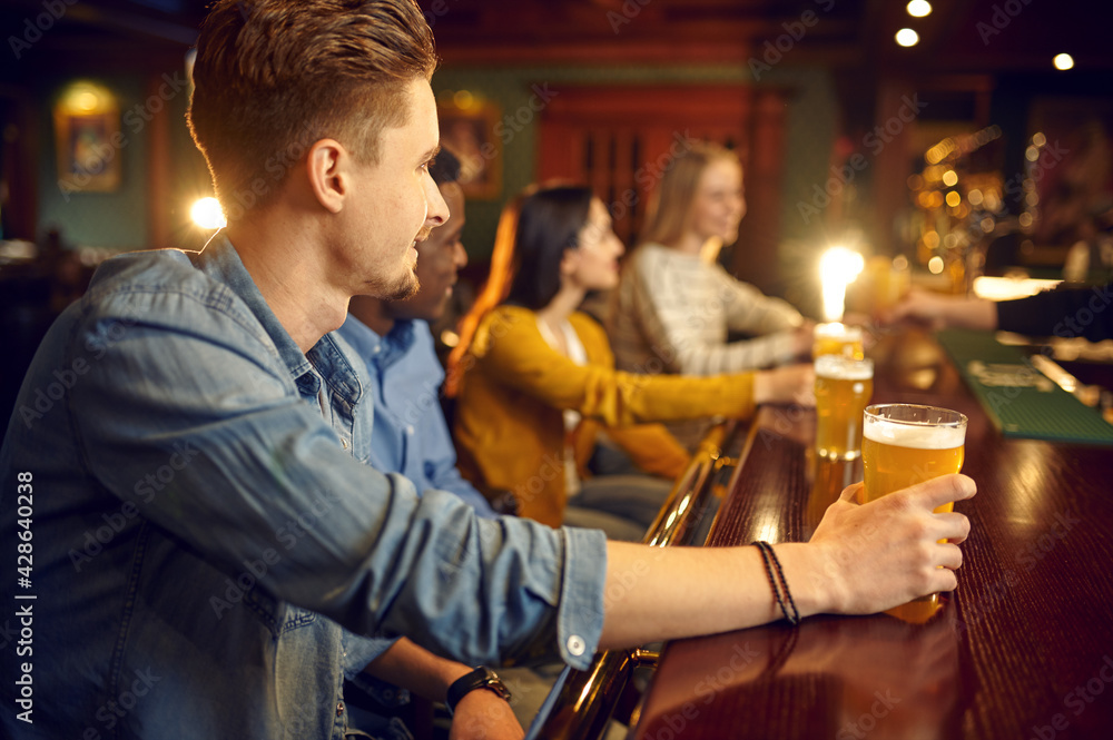 Cheerful friends drinks beer at the counter in bar