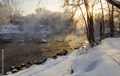 The rays of the sun break through the winter branches of the trees on the bank of the river with fog. the bitter cold of minus 30 degrees Celsius. © vladimircaribb