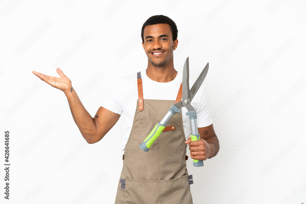 African American gardener man holding pruning shears over isolated white background extending hands to the side for inviting to come African American gardener man holding pruning shears over isolated white background extending hands to the side for inviting to come