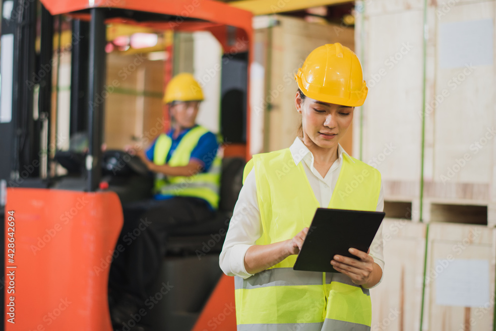 Young Asian woman worker use tablet to check stock in big warehouse factory store which smile and felling happy, old man drive forklift to transport box back side, logistic and transportation concept Young Asian woman worker use tablet to check stock in big warehouse factory store which smile and felling happy, old man drive forklift to transport box back side, logistic and transportation concept