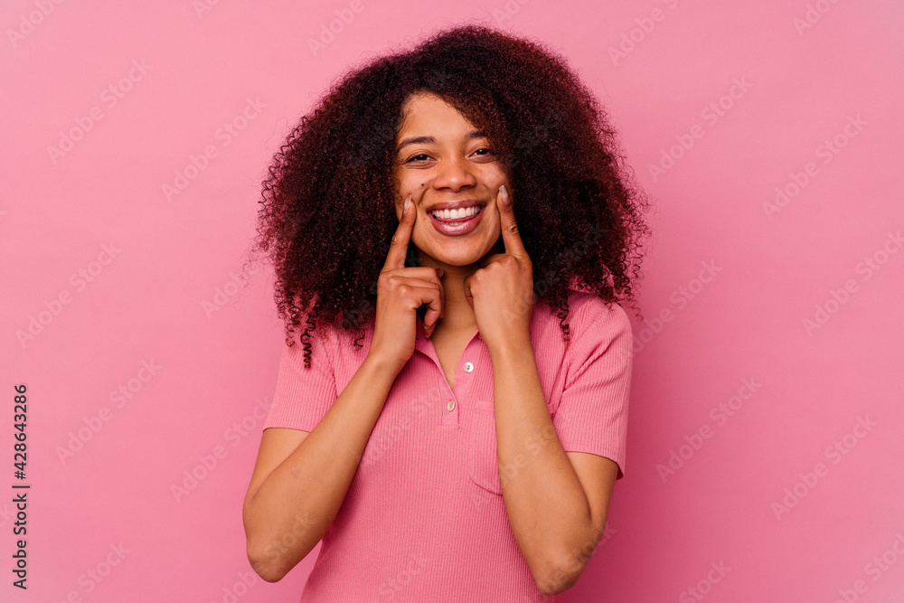 Young african american woman isolated on pink background smiles, pointing fingers at mouth. Young african american woman isolated on pink background smiles, pointing fingers at mouth.
