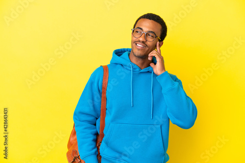 African American student man over isolated yellow background thinking an idea while looking up