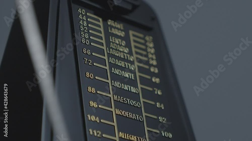 Close up shot of a mechanical metronome, showing the needle moving, gold and black design.