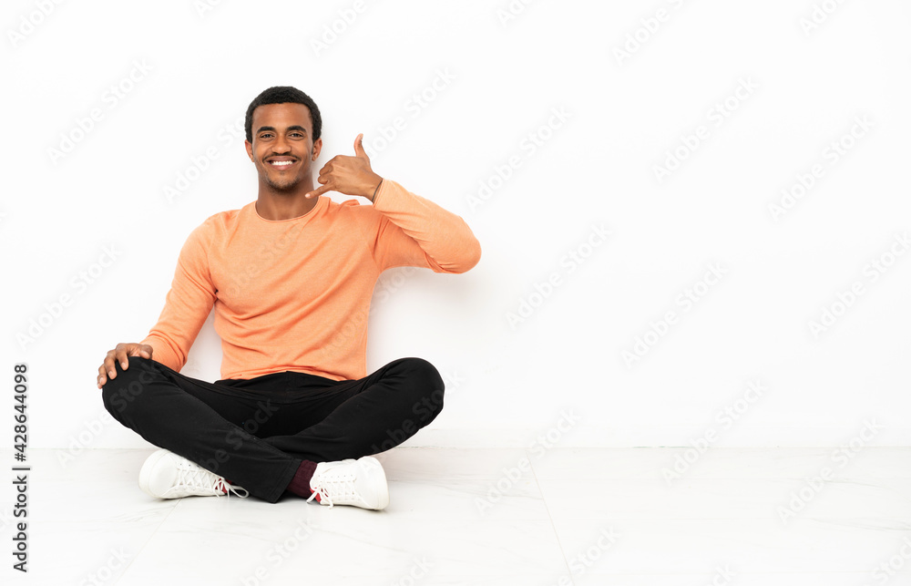 African American man sitting on the floor over isolated copyspace background making phone gesture. Call me back sign African American man sitting on the floor over isolated copyspace background making phone gesture. Call me back sign