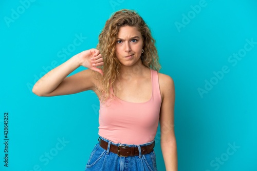 Young blonde woman isolated on blue background showing thumb down with negative expression