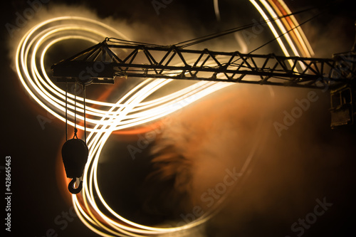 Abstract Industrial background with construction crane silhouette over amazing night sky with fog and backlight. Tower crane against the foggy sky at night.