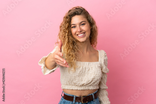 Young blonde woman isolated on pink background shaking hands for closing a good deal
