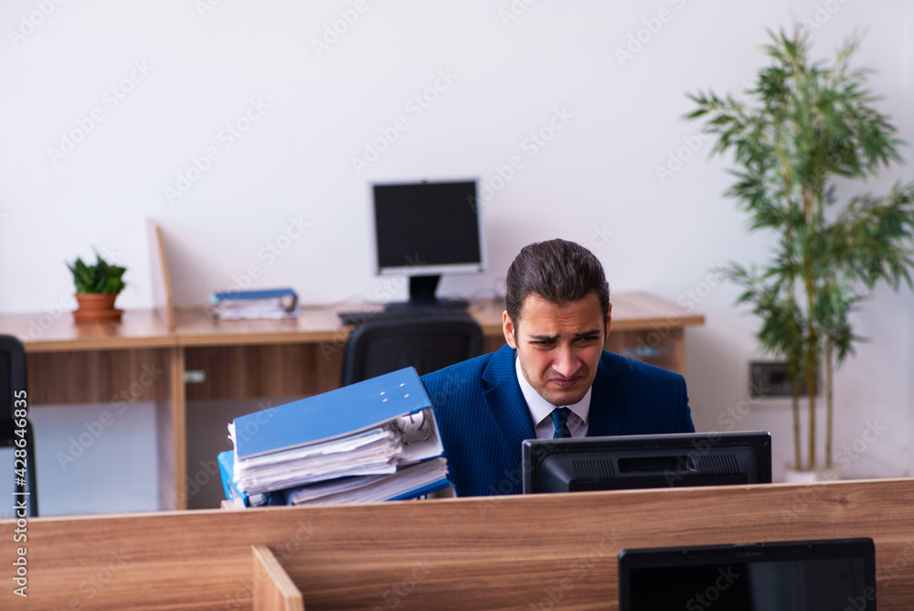 Young male employee unhappy with excessive work in the office Young male employee unhappy with excessive work in the office