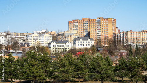 Village houses on a hill against a blue sky. Meadow with trees and grass in the field in front of the house. Horizontal village landscape with summer sunny day.