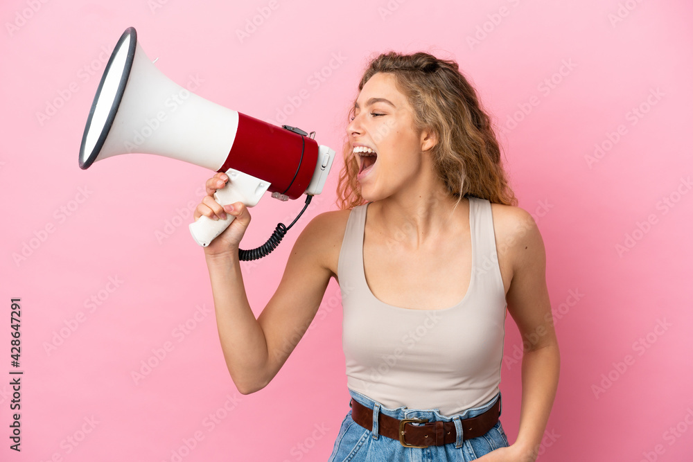 Young blonde woman isolated on pink background shouting through a megaphone to announce something in lateral position Young blonde woman isolated on pink background shouting through a megaphone to announce something in lateral position