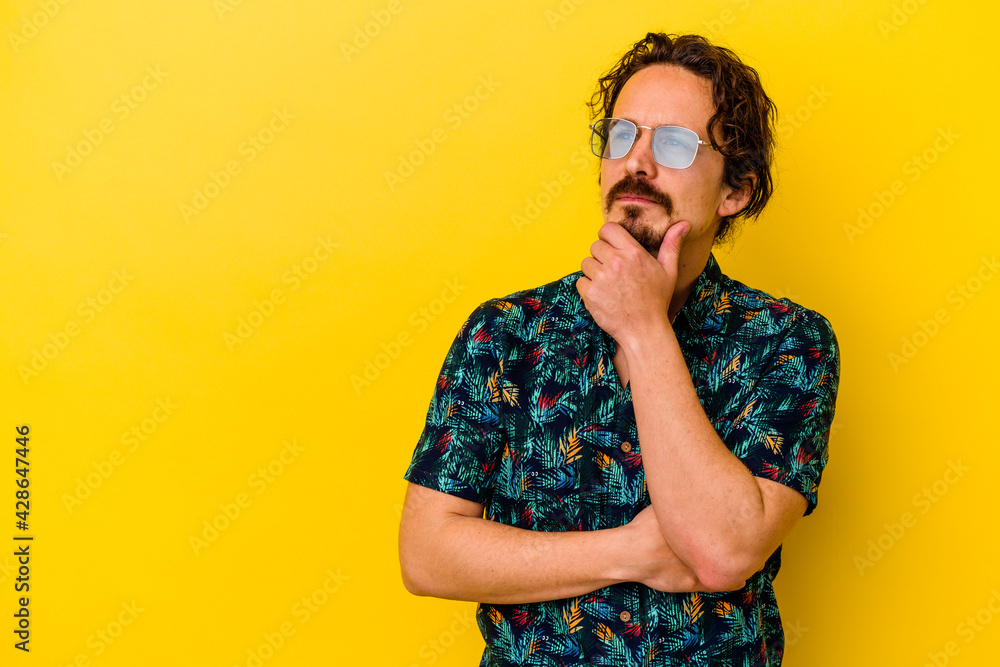 Young caucasian man wearing summer clothes isolated on yellow background looking sideways with doubtful and skeptical expression. Young caucasian man wearing summer clothes isolated on yellow background looking sideways with doubtful and skeptical expression.