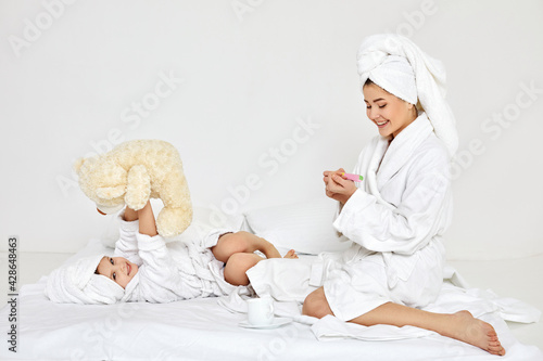 mother making manicure and daughter playing with teddy bear