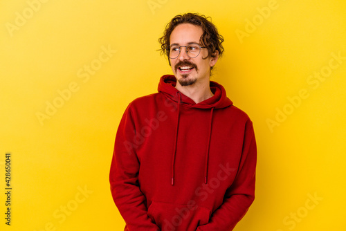 Young caucasian man isolated on yellow background looks aside smiling, cheerful and pleasant. © Asier