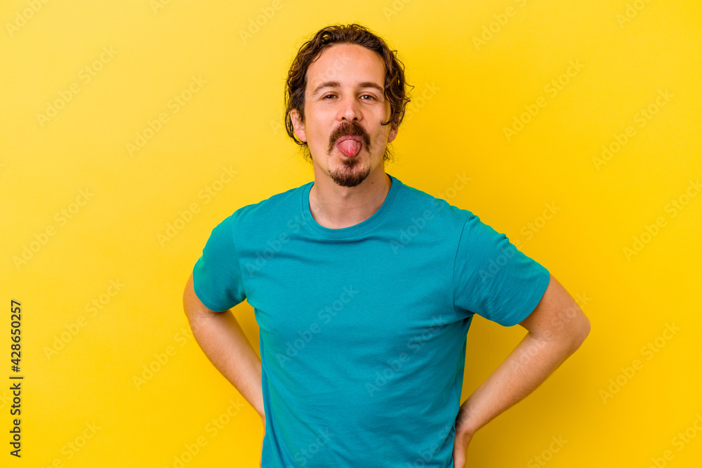 Young caucasian man isolated on yellow background funny and friendly sticking out tongue. Young caucasian man isolated on yellow background funny and friendly sticking out tongue.