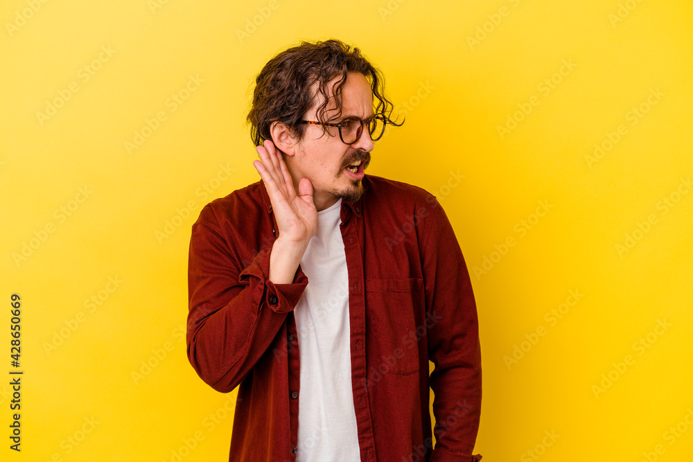 Young caucasian man isolated on yellow background trying to listening a gossip. Young caucasian man isolated on yellow background trying to listening a gossip.