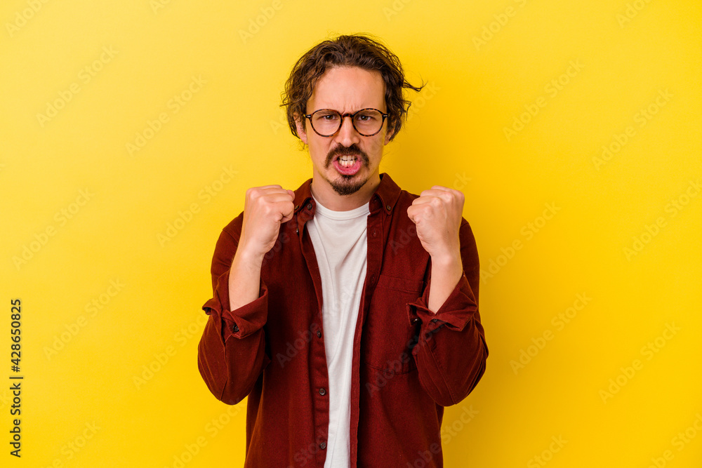 Young caucasian man isolated on yellow background showing fist to camera, aggressive facial expression. Young caucasian man isolated on yellow background showing fist to camera, aggressive facial expression.