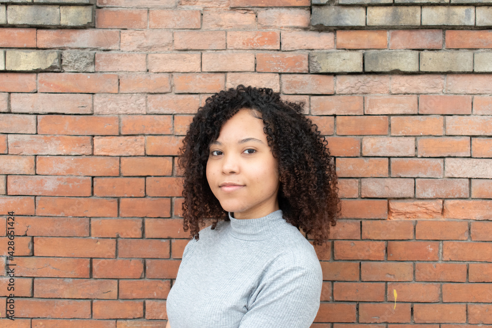young curly-haired girl looking directly into the camera with a red brick wall behind her. young curly-haired girl looking directly into the camera with a red brick wall behind her.