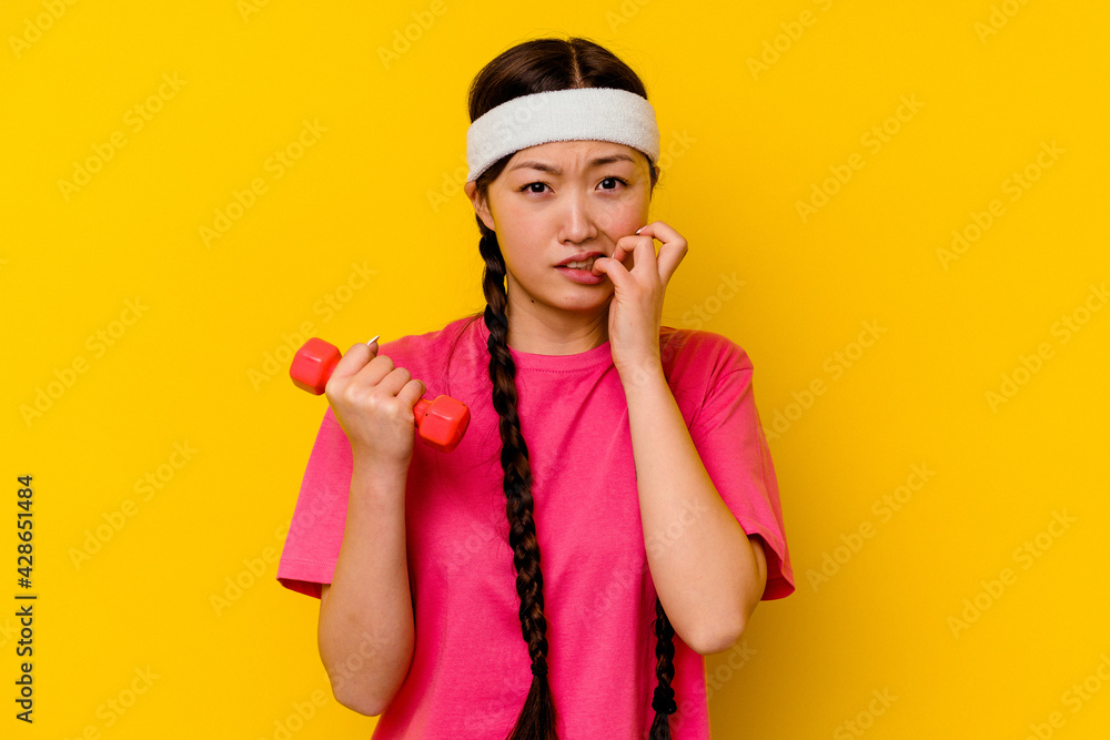 Young sport chinese woman isolated on yellow background biting fingernails, nervous and very anxious. Young sport chinese woman isolated on yellow background biting fingernails, nervous and very anxious.