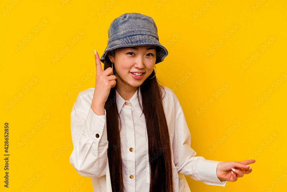 Young chinese woman isolated on yellow background pointing to different copy spaces, choosing one of them, showing with finger. Young chinese woman isolated on yellow background pointing to different copy spaces, choosing one of them, showing with finger.