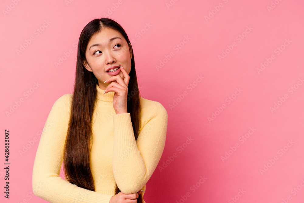 Young chinese woman isolated on pink background relaxed thinking about something looking at a copy space. Young chinese woman isolated on pink background relaxed thinking about something looking at a copy space.