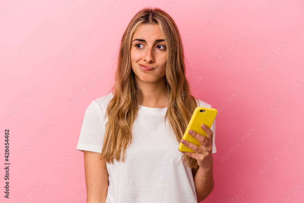 Young blonde caucasian woman holding a yellow mobile phone isolated confused, feels doubtful and unsure. Young blonde caucasian woman holding a yellow mobile phone isolated confused, feels doubtful and unsure.