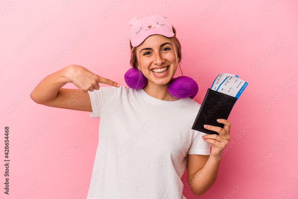 Young caucasian blonde woman holding a passport and tickets to travel isolated on pink background person pointing by hand to a shirt copy space, proud and confident Young caucasian blonde woman holding a passport and tickets to travel isolated on pink background person pointing by hand to a shirt copy space, proud and confident